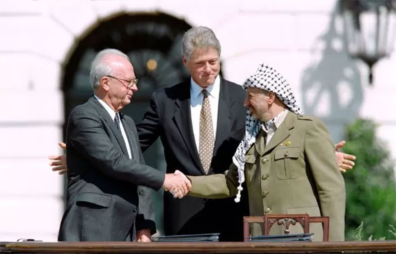 Jabat tangan antara Perdana Menteri Israel Yitzhak Rabin (kiri) dan kepala Organisasi Pembebasan Palestina Yasser Arafat (kanan) dengan Presiden Amerika Serikat Bill Clinton di tengah.