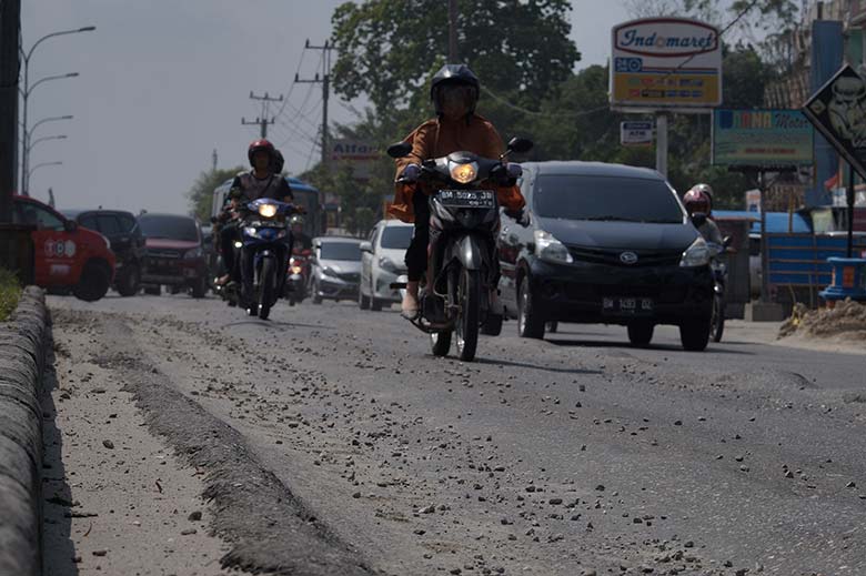 BERGELOMBANG: Kendaraan melintasi jalan bergelombang dan penuh dengan kerikil di Jalan HR Soebrantas, Pekanbaru, Selasa (14/7/2019). Pengendara mesti berhati-hati mellintasi jalan tersebut akibat kondisi jalan yang belum diperbaiki.
