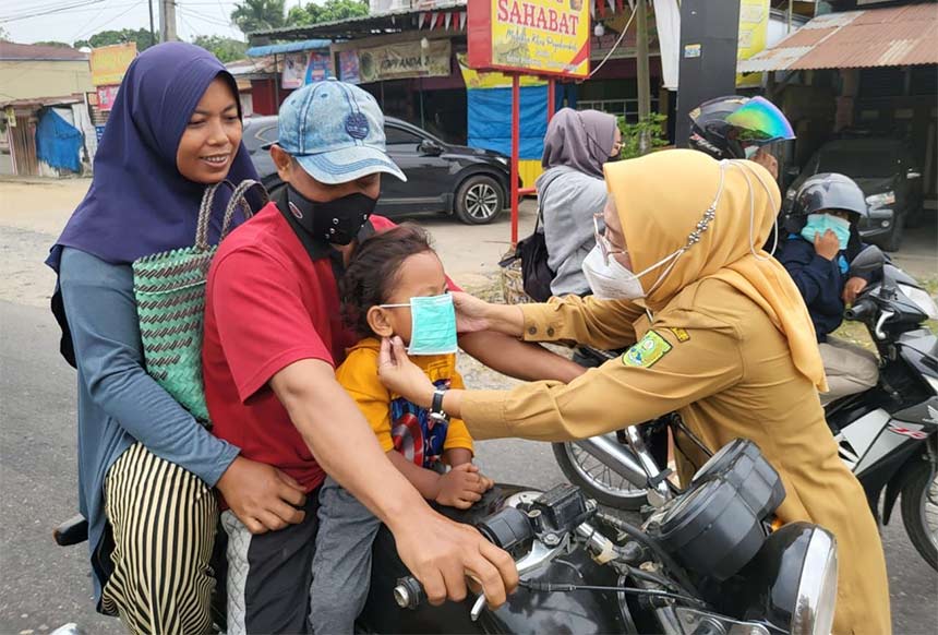 Kepala Diskes Inhu, Elis Julinarti DCN Mkes memasangkan masker kepada salah seorang anak yang melintas bersama orangtuanya di Simpang Empat Tugu Ikan Patin Kelurahan Pematang Reba, Senin (9/10/2023)