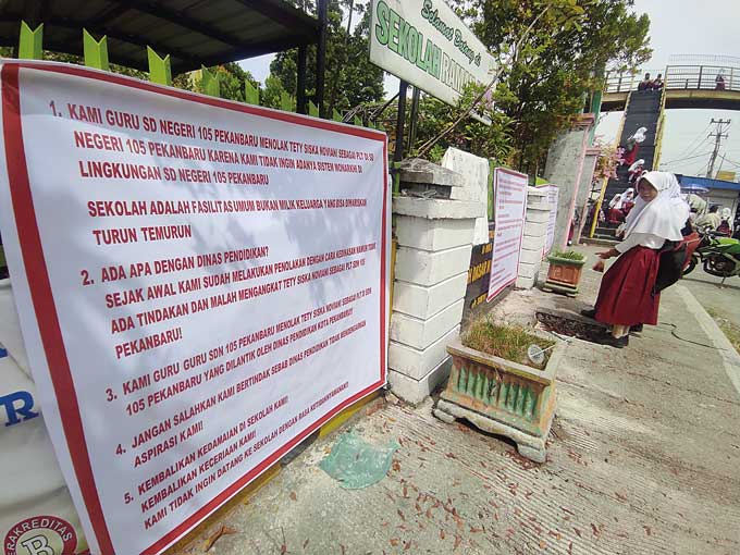 Sejumlah murid berdiri di depan spanduk  yang bertuliskan protes guru pengajar terhadap penunjukan Plt Kepala SDN 105 Pekanbaru, Jalan HR Soebrantas pada hari pertama masuk sekolah tahun ajaran baru 2022/2023,Senin (11/7/2022).