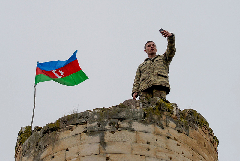 Seorang tentara Azerbaijan foto bersama bendera negaranya yang dikibarkan di Lachin, wilayah terakhir di Nagorno-Karabakh yang diserahkan oleh pihak Armenia. (AFP/DAILY SABAH)