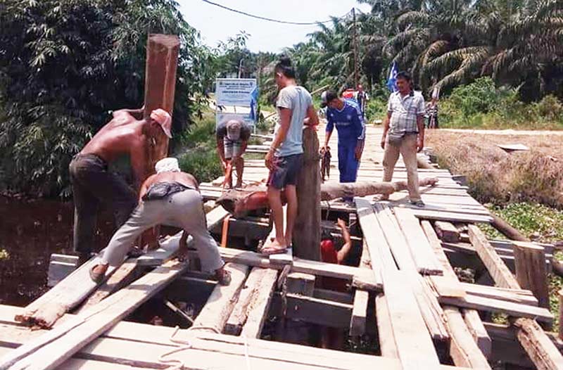 DIPERBAIKI: Warga memperbaiki jembatan kayu yang menghubungkan Jalan Garuda dan Bukit Cahaya, Kecamatan Dumai Selatan, Ahad (7/4/2019).