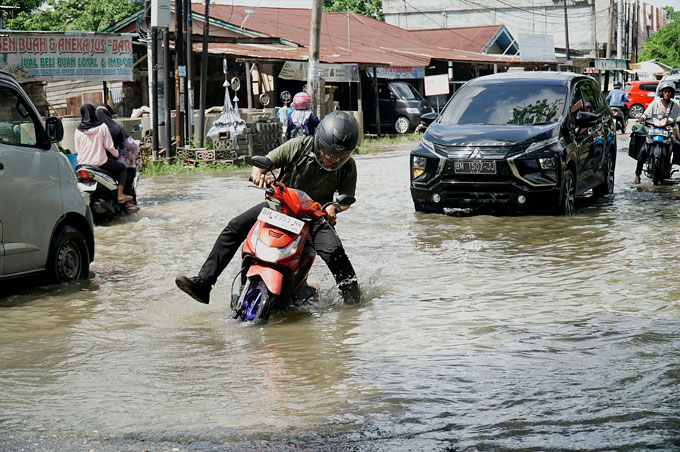 Seorang pengendara sepeda motor hampir terjatuh saat menerobos genangan air di Jalan Cipta Karya, Kecamatan Tuah Madani, Jumat (17/11/2023) pagi. Genangan air terjadi saat hujan deras turun dan tidak adanya saluran air yang memadai di pinggir Jalan Cipta