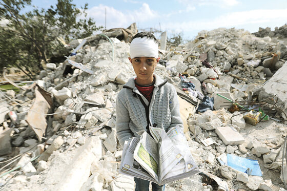 Seorang bocah Suriah yang kehilangan seluruh anggota keluarga membawa buku di tengah puing bekas rumahnya di Aleppo, paska gempa Turki-Suriah.