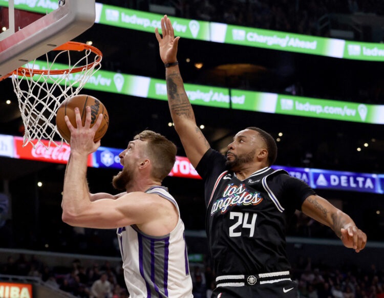 Domantas Sabonis dari Sacramento Kings (kiri) mencetak poin melewati hadangan Norman Powell (LA Clippers) pada laga di Crypto.com Arena, Sabtu (25/2/2023).