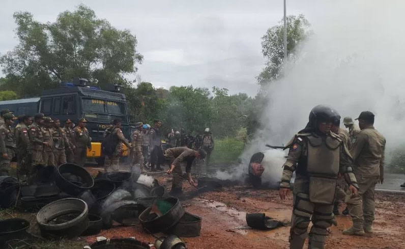 Petugas gabungan membersihkan tumpukan ban yang dibakar warga di lokasi bentrokan di Rempang, Batam.
