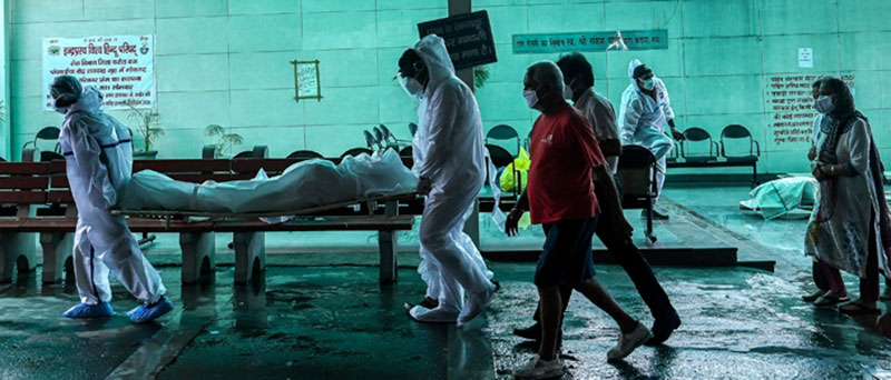 Satu keluarga dengan menggunakan APD menggotong sendiri jenazah anggota keluarga mereka yang meninggal akibat Covid-19 di krematorium di New Delhi.