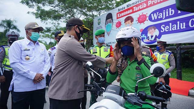 Kapolres Siak AKBP Doddy F Sanjaya menyerahkan masker kepada pengendara sepeda motor disaksikan Bupati Siak Drs H Alfedri di bundaran Jembatan Tengku Agung Sultanah Latifah Siak, Rabu (17/6/2020). Monang Lubis/Riau Pos