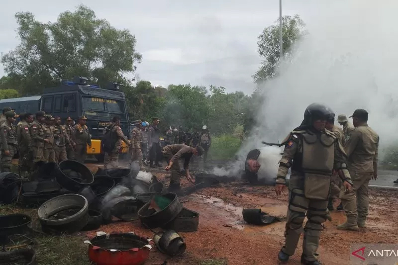 Petugas gabungan membersihkan tumpukan ban yang dibakar warga di lokasi bentrokan di Rempang, Batam.