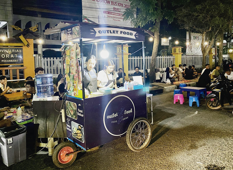 Pedagang sibuk mempersiapkan makanan dengan latar pengunjung duduk lesehan di trotoar Madani Street Food di Jalan Cut Nyak Dhien, Sabtu (21/10/2023) malam.