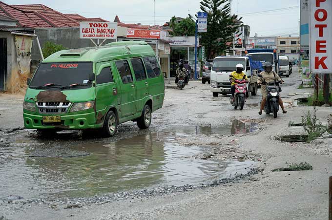 Kendaraan bermotor melintas di Jalan Suka Karya/Jalan Kualu,  Kecamatan Tuah Madani yang rusak parah dan tergenang air, Selasa (24/1/2023). Kondisi jalan yang rusak sampai saat ini belum dilakukan perbaikan oleh pihak terkait.