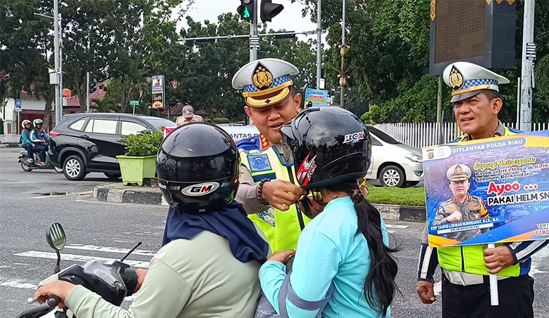 Dirlantas Polda Riau Kombes Pol Taufiq Lukman memasangkan helm kepada penumpang roda dua di Jalan Diponegoro, Pekanbaru, Selasa (14/11/2023).