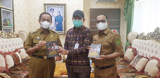 Bupati Inhil HM Wardan didampingi Kadiskominfopers Inhil Trio Beni Putra, menerima buku dari Ketua KI Riau, Zufra Irwan, Senin (20/9/2021).