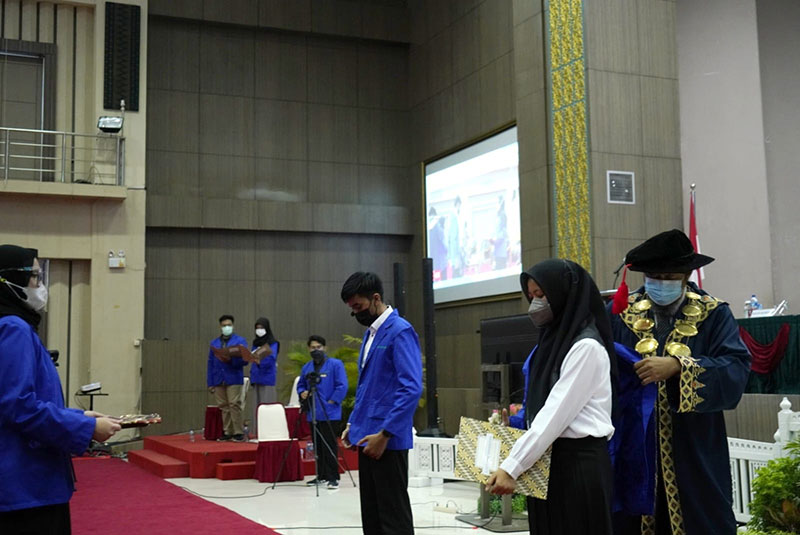 Direktur Politeknik Caltex Riau Dr Mohammad Yanuar H ST MT memasangkan almamater kepada perwakilan mahasiswa baru yang hadir secara luring saat pelantikan mahasiswa baru Politeknik Caltex Riau tahun 2021.