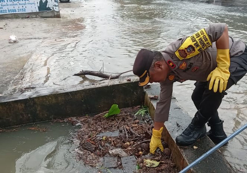 Kapolsek Tenayan Raya Kompol Oka Mahendra Syahrial mengecek sumbatan dan tumpukan sampah di drainase yang tidak jauh dari titik genangan air di Jalan Bukit Barisan, Kamis (21/12/2023).