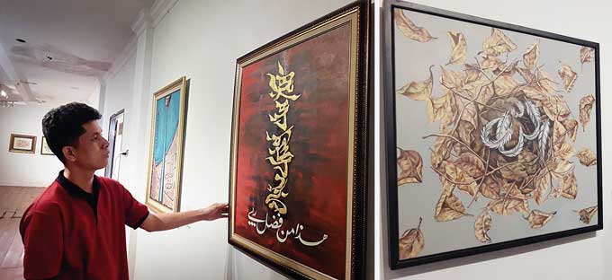 Pengurus Galeri Hang Nadim Yelmi Nanda Resfi saat menjelaskan lukisan kaligrafi karya seniman lokal Riau yang dipajang dalam Pameran Kaligrafi Kontemporer di Lantai 2 Anjungan Kampar, Kompleks Bandar Seni Raja Ali Haji (Serai), Kamis (2/3/2023).