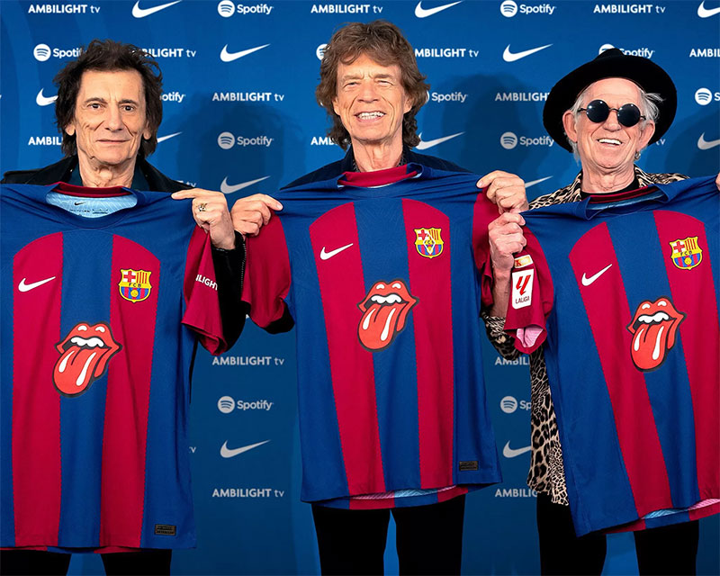 Tiga personel Rolling Stones memamerkan jersey Barcelona bergambar lidah menjulur.
