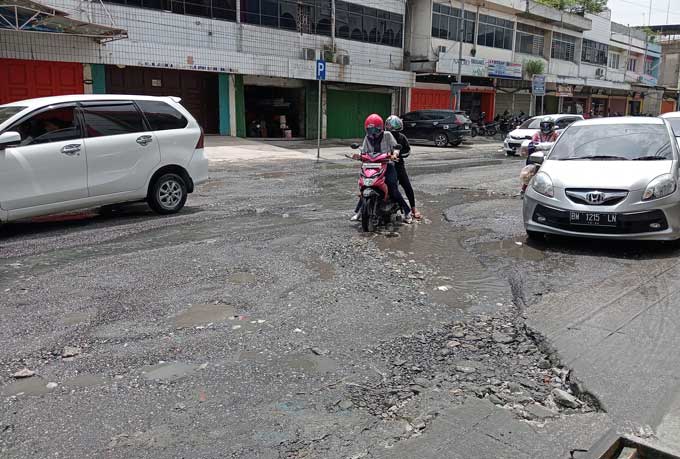 Pengendara sepeda motor kesulitan saat kendaÂ­raannya tersangkut di lubang yang ada di Jalan Juanda, Selasa (21/2/2023).