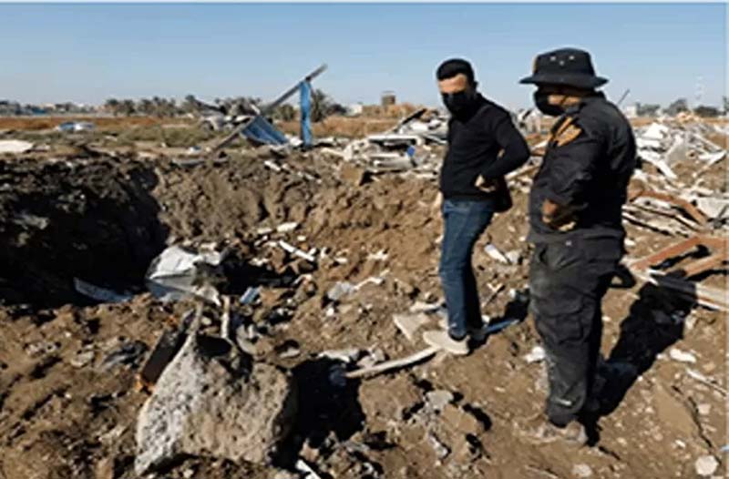 Seorang pejuang kelompok milisi Kataib Hizbullah Irak dan seorang pria memeriksa lokasi serangan udara AS di Hilla, Irak, Selasa (26 /12/2023).