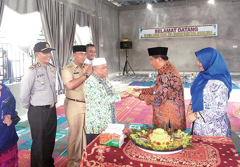 HUT KE-12: Sekda Rohul H Abdul Haris menyerahkan potongan nasi tumpeng kepada Kades Lubuk Napal H Syofian saat menghadiri puncak HUT Ke-12 Desa Lubuk Napal di halaman kantor desa, Selasa (17/12/2019). (humas pemkab rohul)