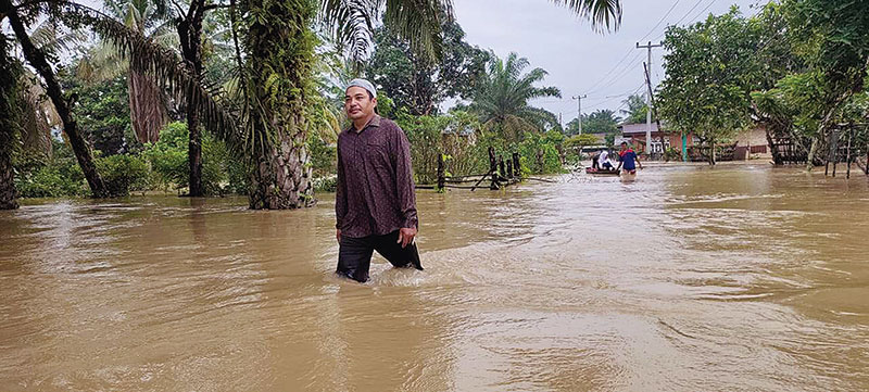 BANJIR: Warga melintasi jalan yang terendam banjir sedalam lutut orang dewasa di Desa Gunung Sahilan, Kecamatan Gunung Sahilan, Kabupaten Kampar, Kamis (12/12/2019). (HENDRAWAN/RIAU POS)